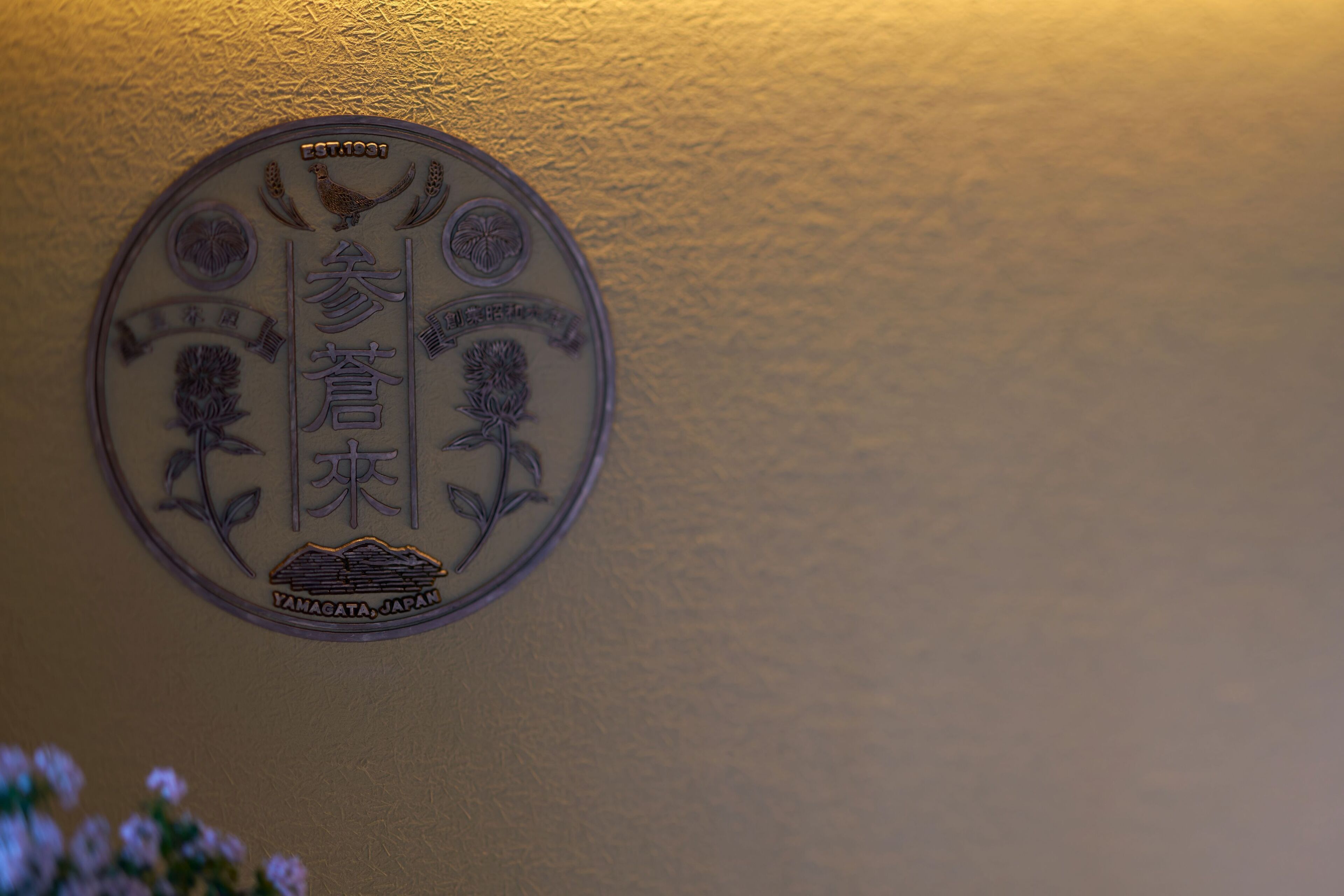 A circular emblem with Japanese characters and a bird, mounted on a textured wall.