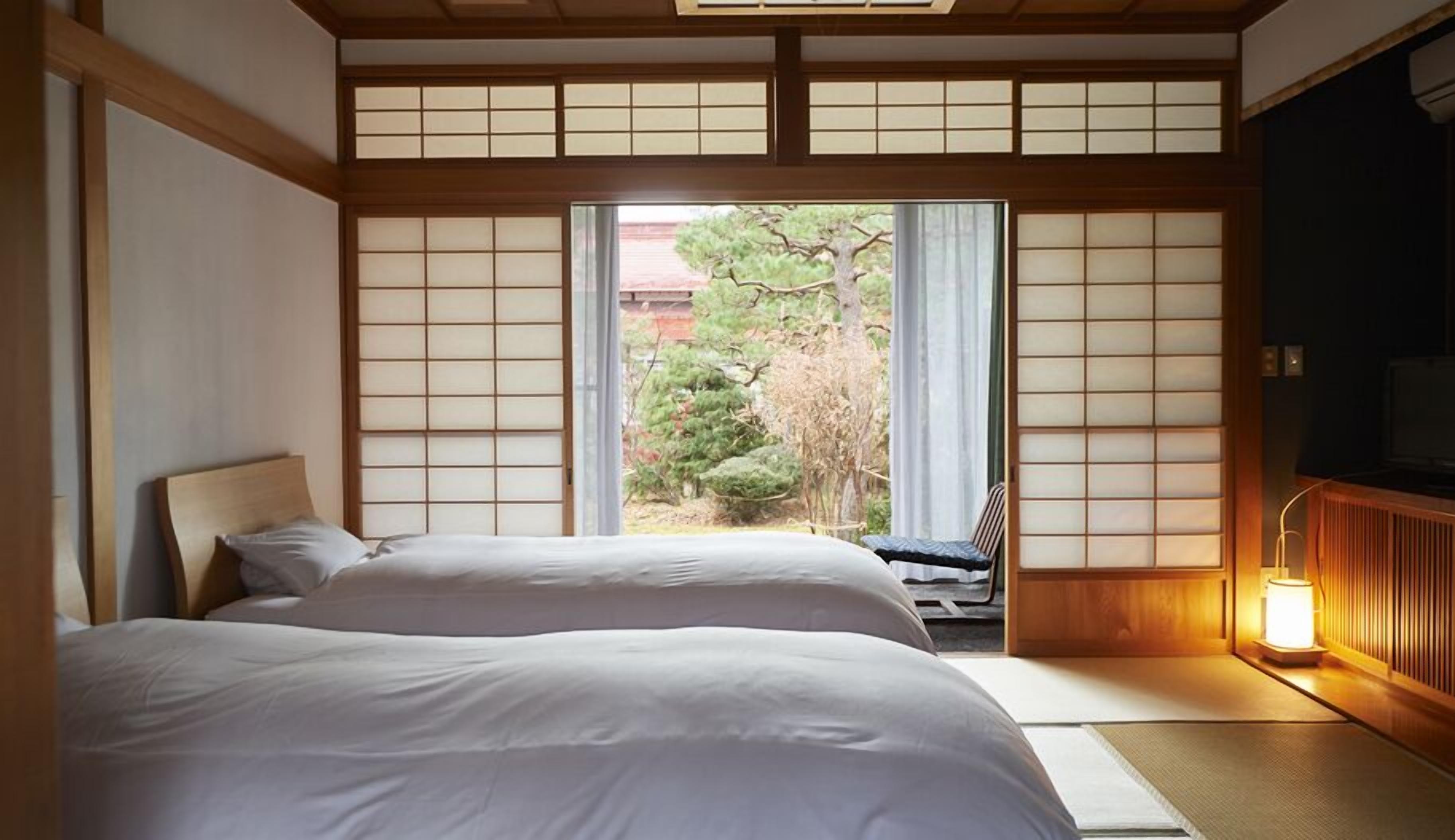 Una habitación tradicional japonesa con suelo de tatami, una cama baja de madera y un puertas correderas que dan a un jardín.