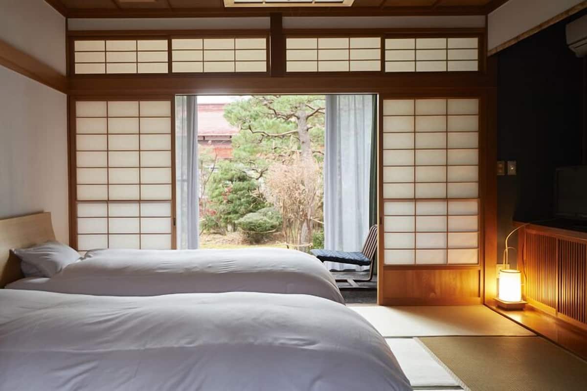 Una habitación tradicional japonesa con suelo de tatami, una cama baja de madera y un puertas correderas que dan a un jardín.