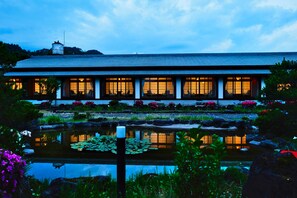 A traditional building with a long roof and multiple windows, surrounded by a garden with a pond and various plants. - Sagiya Sensorai (Kaminoyama)