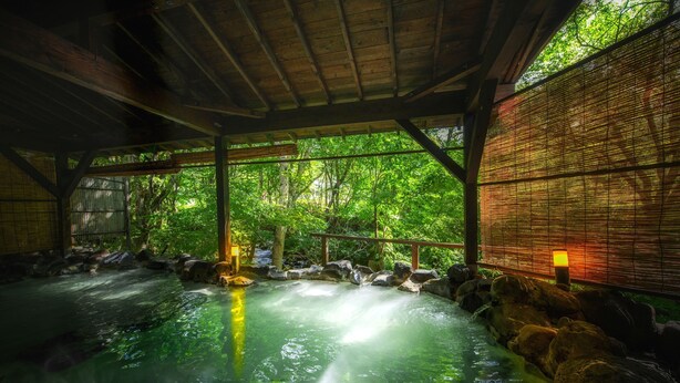 Un onsen japonés tradicional con interior de madera, un baño de piedra y una celosía de bambú.