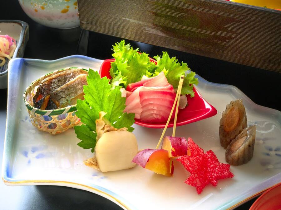 A plate with various food items including a wrapped item, leafy greens, and a red garnish.