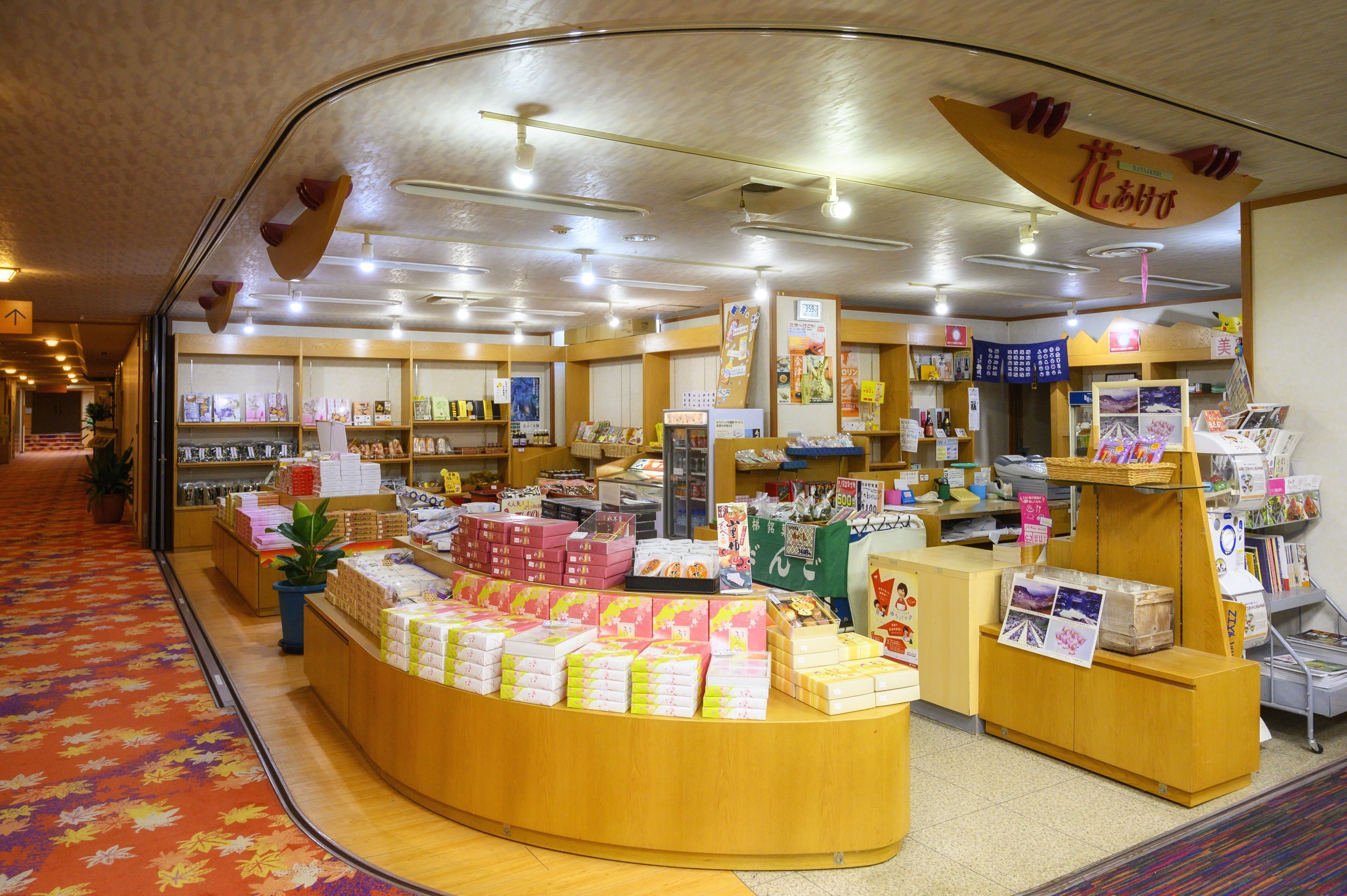 A bookstore with a curved counter displaying various books and magazines. Shelves are stocked with books and other items.