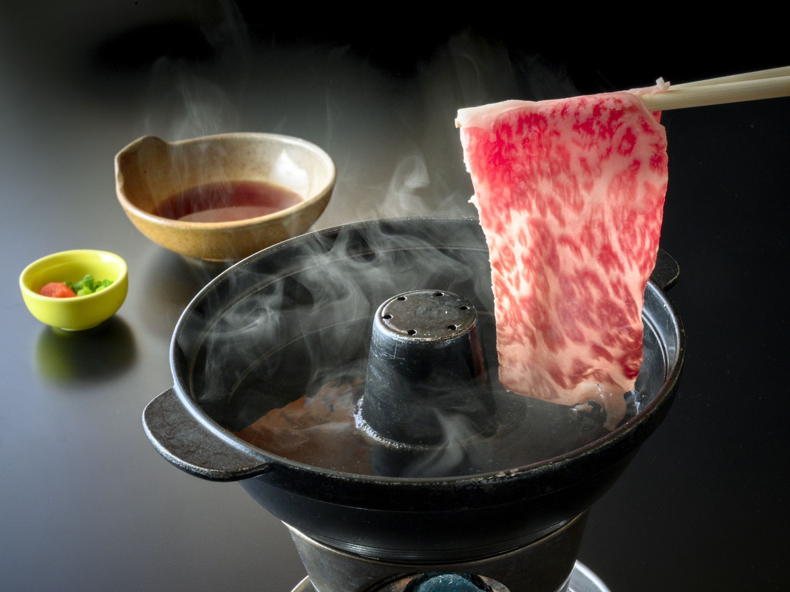 A hot pot with steam rising from it, a wooden bowl, and a small green bowl with vegetables.