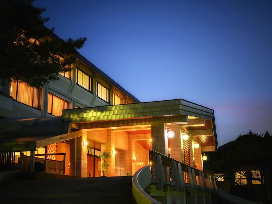 Et moderne hotel med en buet indgang, mange vinduer og en trappe, der fører til indgangen.