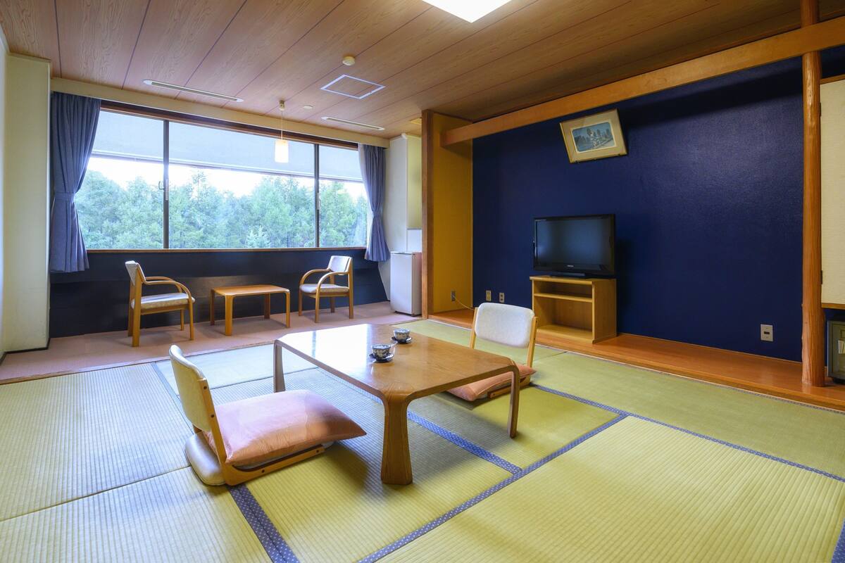 Une pièce de style japonais traditionnel, avec un sol recouvert de tatamis, une petite table en bois et un téléviseur posé sur un meuble.
