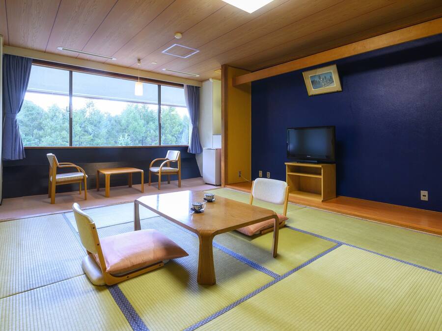 A traditional Japanese room with tatami flooring, a low wooden table, and a television on a stand.