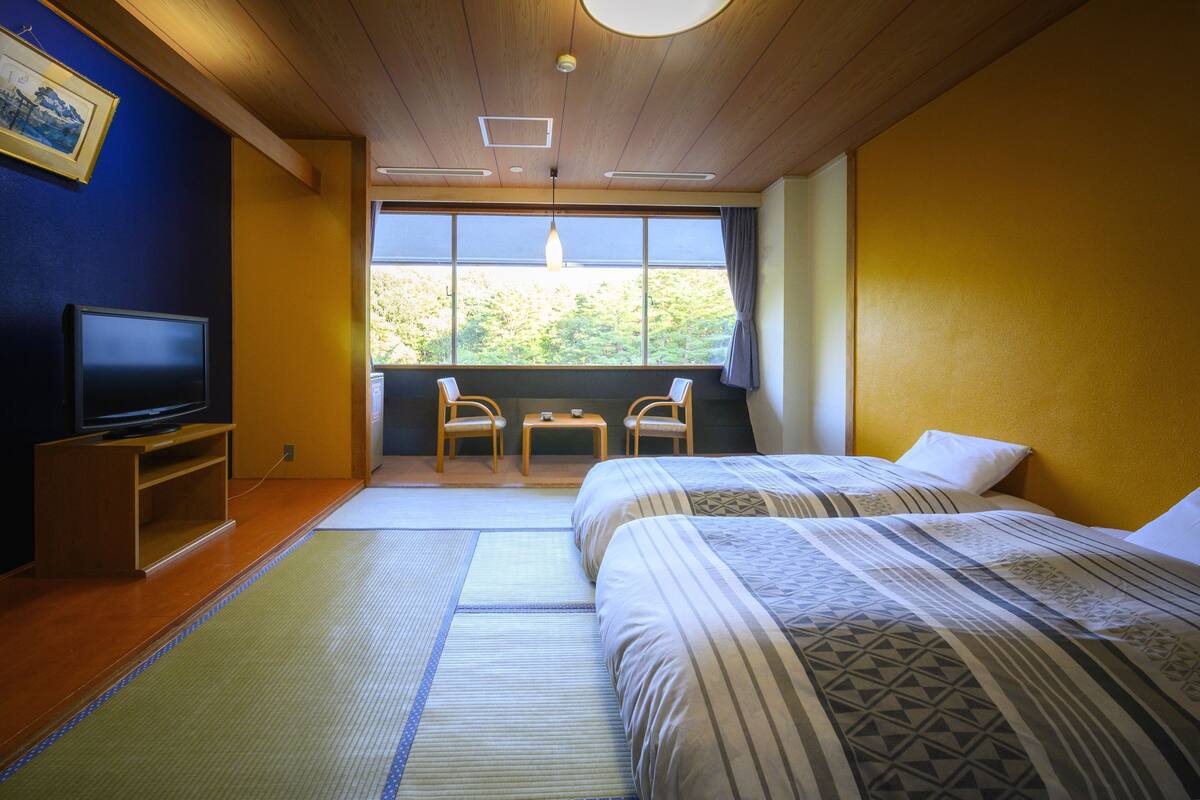 Une chambre d’hôtel avec deux lits, une télévision, une petite table et une fenêtre donnant sur les arbres.