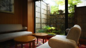 Habitación con un sofá, dos mesitas y vistas a una valla de bambú y follaje exterior.