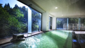 Una piscina con paredes de vidrio transparente, rodeada por un interior moderno con techo de madera y vistas a árboles.