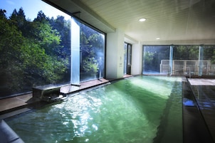 Piscina com paredes de vidro transparente, cercada por um interior moderno com teto de madeira e vista para árvores lá fora.