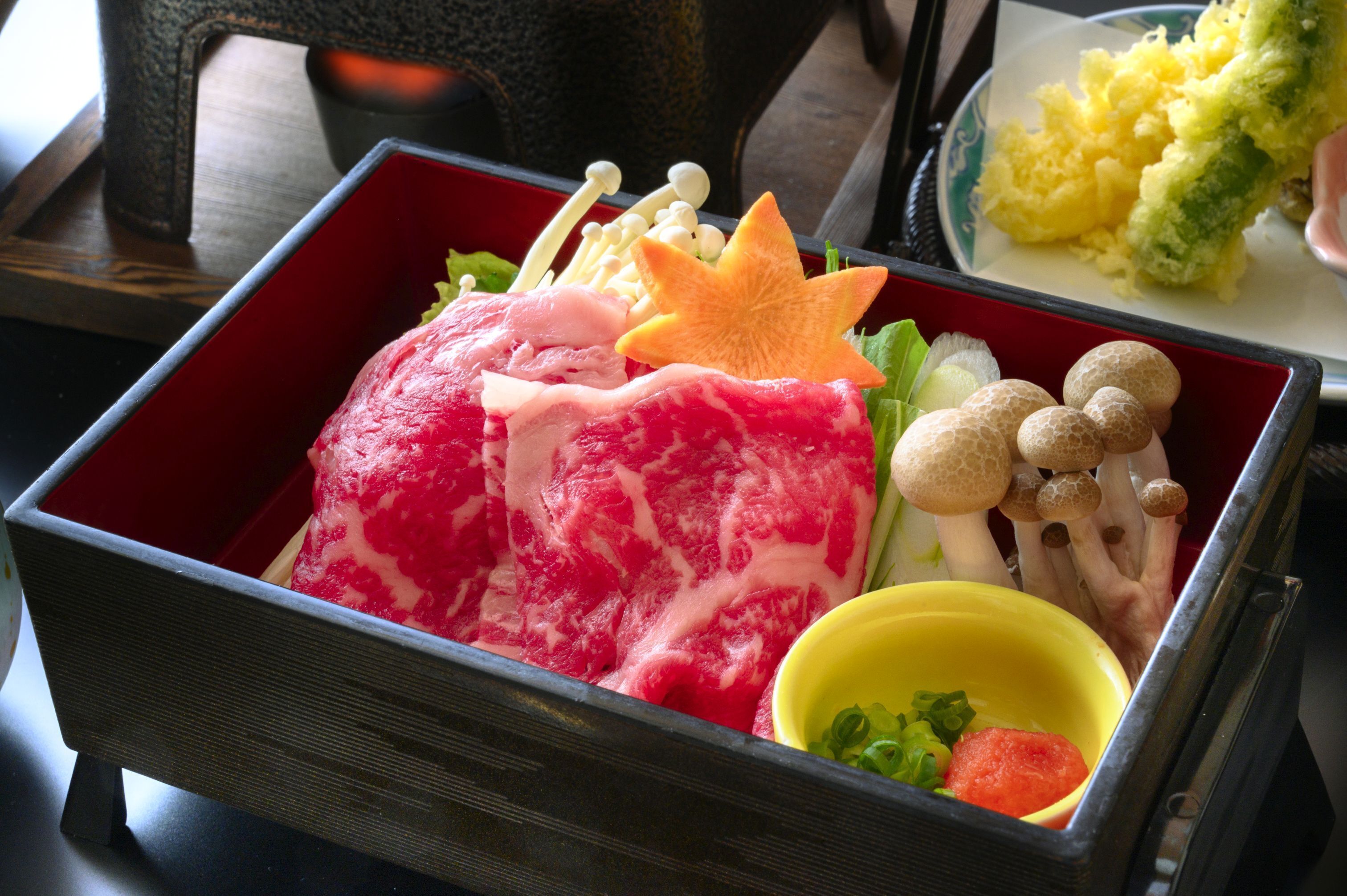 A traditional Japanese bento box with various food items including fish, vegetables, and mushrooms.