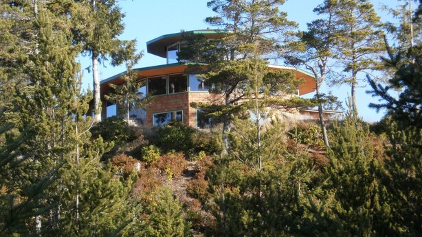 A modern, multi-story building surrounded by dense forest. - Hilltop ocean view round house (Florence)