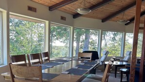 A spacious room with a large wooden table and chairs, large windows offering a view of trees, and a high ceiling with exposed beams. - Hilltop ocean view round house (Florence)