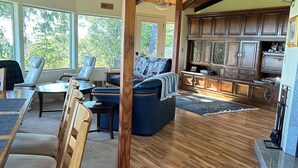 A spacious living room with wooden flooring, a large sofa, and a dining area with chairs. - Hilltop ocean view round house (Florence)