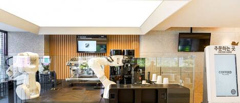 A modern coffee shop with a robotic arm, a coffee machine, and a digital menu display.