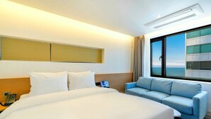 A hotel room with a large bed, a sofa, a bedside table with a phone, and a window with a view of a building. - Haeundae Thevan Hotel (Busan)