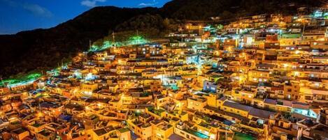 Un pueblo en la ladera, densamente poblado y bellamente iluminado por numerosas construcciones, de noche.