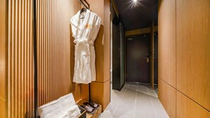 A hallway with wooden paneling, a robe hanging on a rack, a towel and shoes on a shelf, and a door at the end. - Haeundae Thevan Hotel (Busan)