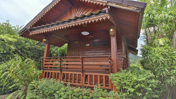 Eine Holzhütte mit geneigtem Dach, umgeben von üppigem Grün.