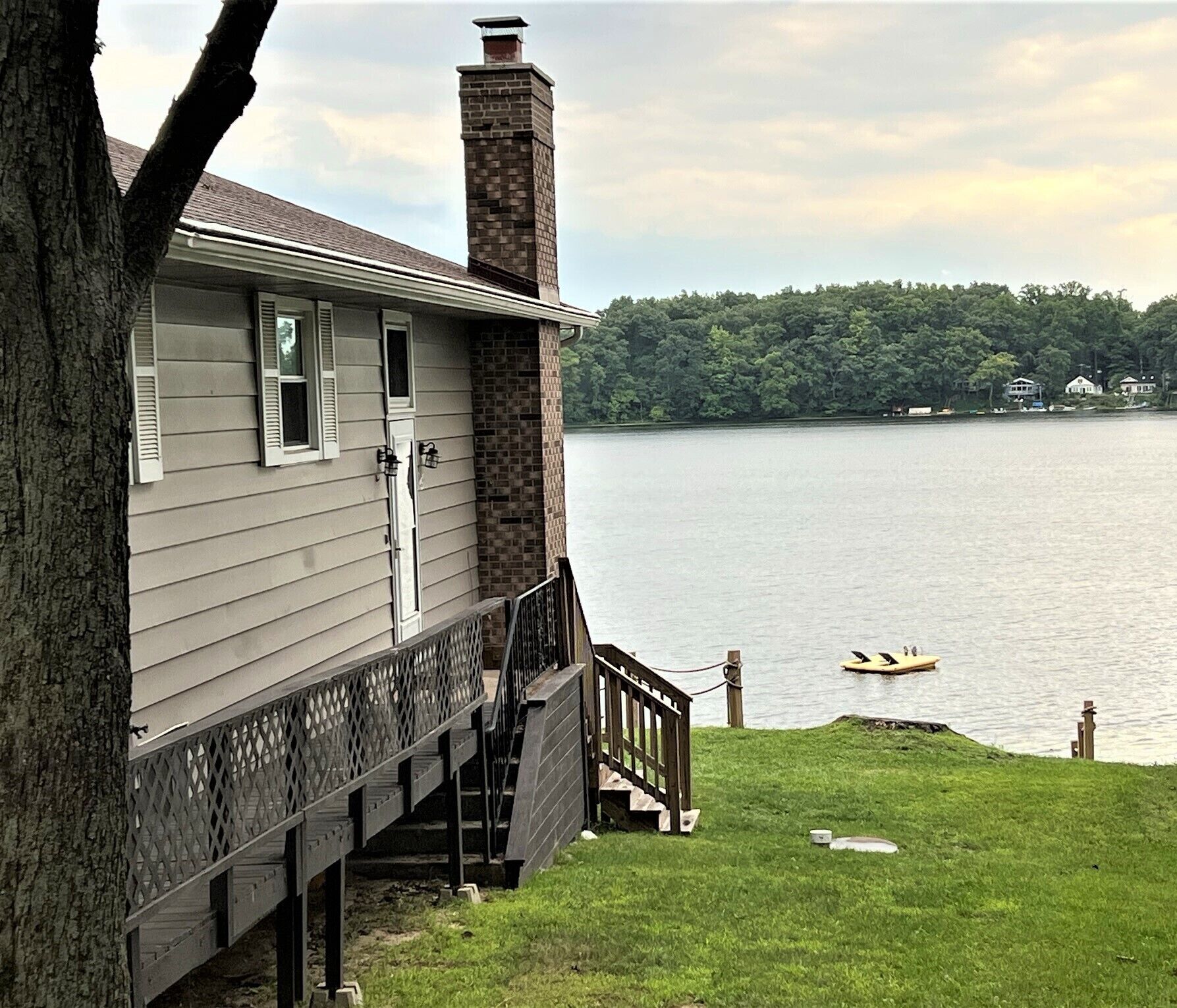 A house with a brick chimney, a wooden deck, and a view of a lake with a boat.