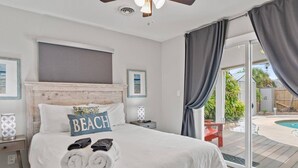 Una camera da letto con un letto, una ventola a soffitto, un comodino e vista su una piscina esterna.