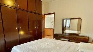 Une chambre à coucher avec une grande armoire, une table de chevet avec un miroir et un lit recouvert d’une couvre-lit à motifs.