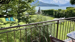Un balcon donnant sur un lac, un espace herbeux avec des chaises et une rambarde en métal.