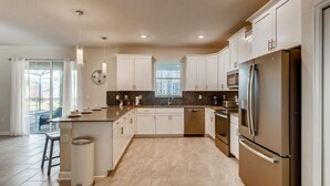 A modern kitchen with white cabinets, a stainless steel refrigerator, and a large island with a sink.