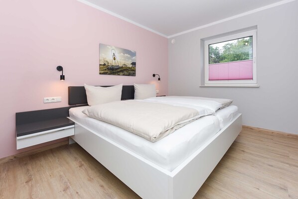 A modern bedroom with a bed, bedside tables, wall-mounted lamps, a window with blinds, and a painting on the wall.