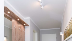 Een gang met een houten garderobe, een witte deur en een witte wandplank.