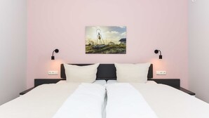 Een net opgemaakt bed met witte lakens, een zwart hoofdbord en een aan de muur bevestigd landschapsbeeld.