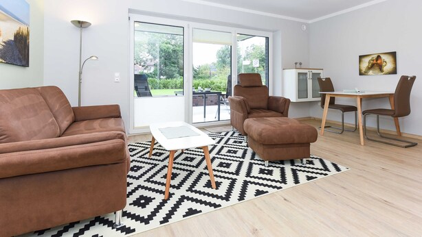 Een moderne woonkamer met een bruine bank, een witte salontafel en een kamerkleed met patroon.