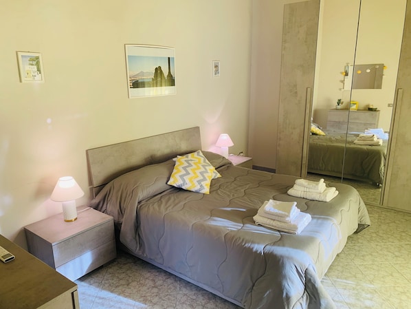 Un dormitorio ordenado con cama, mesitas de noche, un espejo y obras de arte en las paredes.