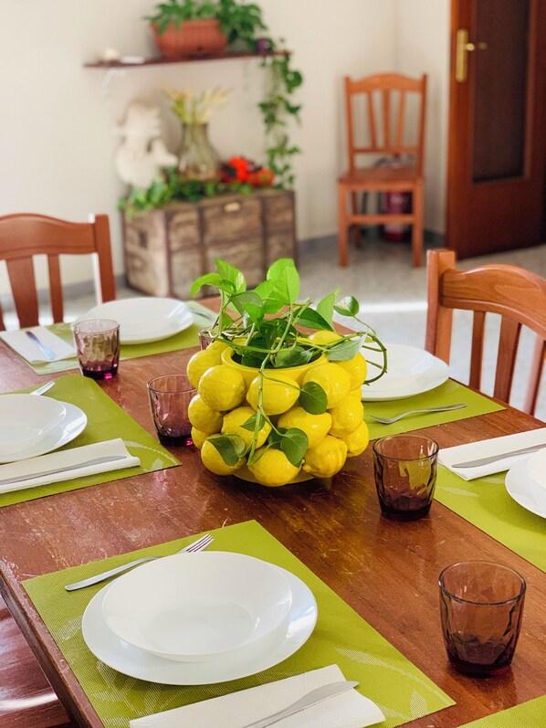 Una mesa de comedor dispuesta con platos, cubiertos y vasos, con un centro de limones y follaje.