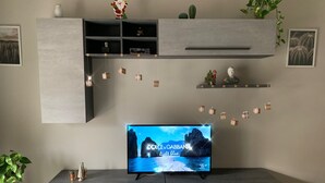 A modern living room with a flat-screen TV on a grey entertainment unit, decorated with small gift boxes and a Santa figurine.