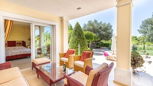 Quarto de hotel com porta de vidro que dá para uma varanda, mobiliado com sofá, cadeiras e mesa.