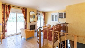 Uma sala de estar ampla com lareira, escada e varanda com cortinas.