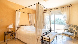 Uma cama com dossel e cortina, um criado-mudo, uma cadeira e vista para o exterior.
