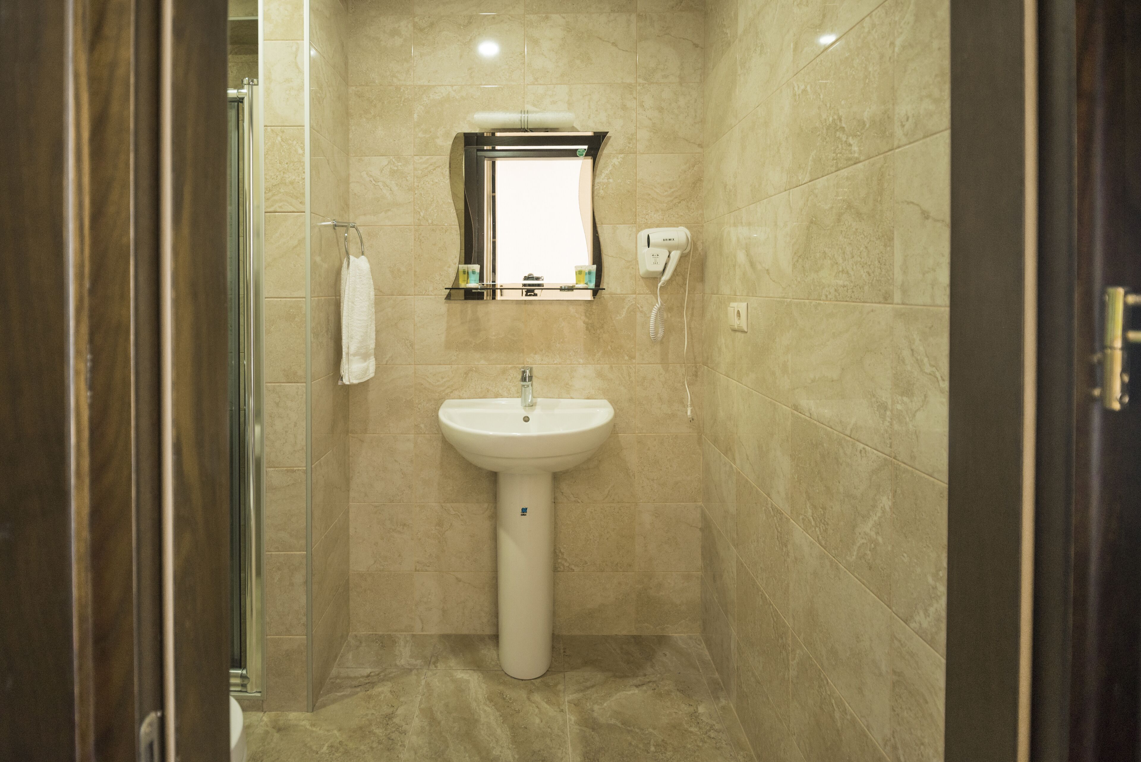 A bathroom with a pedestal sink, a mirror, and a hand dryer.