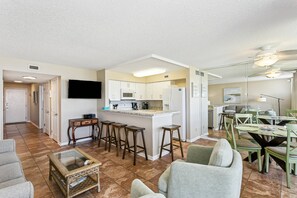 Une cuisine moderne dotée d’un îlot central, de tabourets de bar et d’un coin repas avec des chaises vertes et une table ronde.