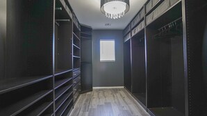 Un dressing accessible sans porte, avec des étagères en bois foncé, un lustre et une fenêtre.