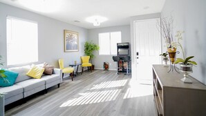 Un salon avec un canapé, deux fauteuils jaunes, une petite table, une plante et une console de jeux.