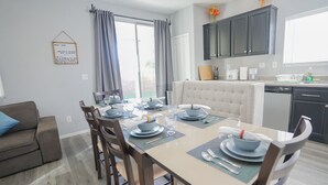 Un coin repas avec une table dressée pour quatre personnes, un canapé et une cuisine dotée de meubles sombres et d’un lave-vaisselle.