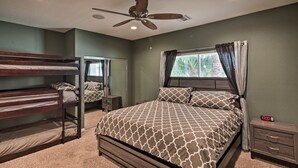 Un dormitorio con literas, una cama con ropa de cama estampada, un ventilador de techo, una mesita de noche y una ventana con cortinas.