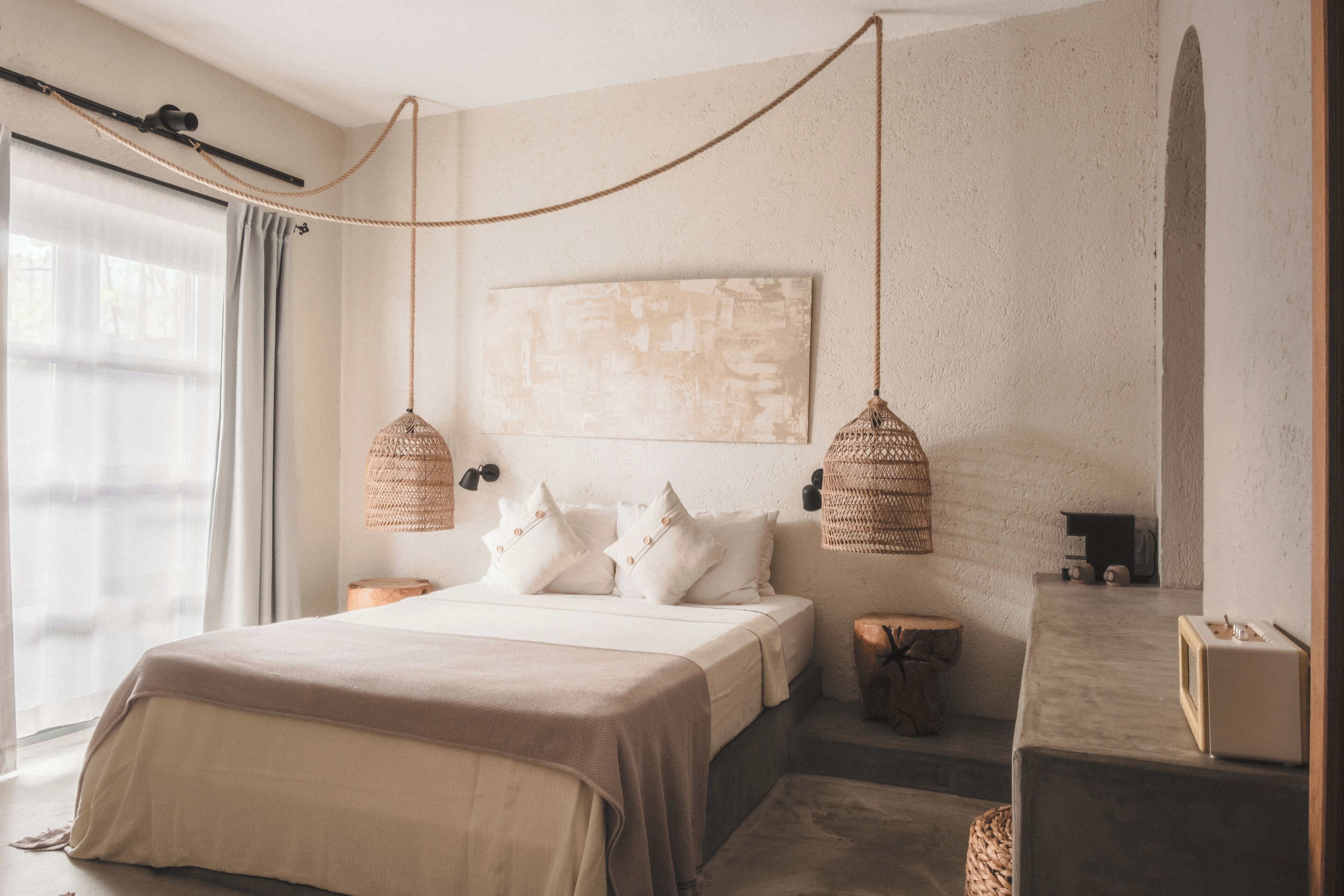 A bedroom with a bed, bedside tables, a hanging light fixture, and a large abstract painting on the wall.