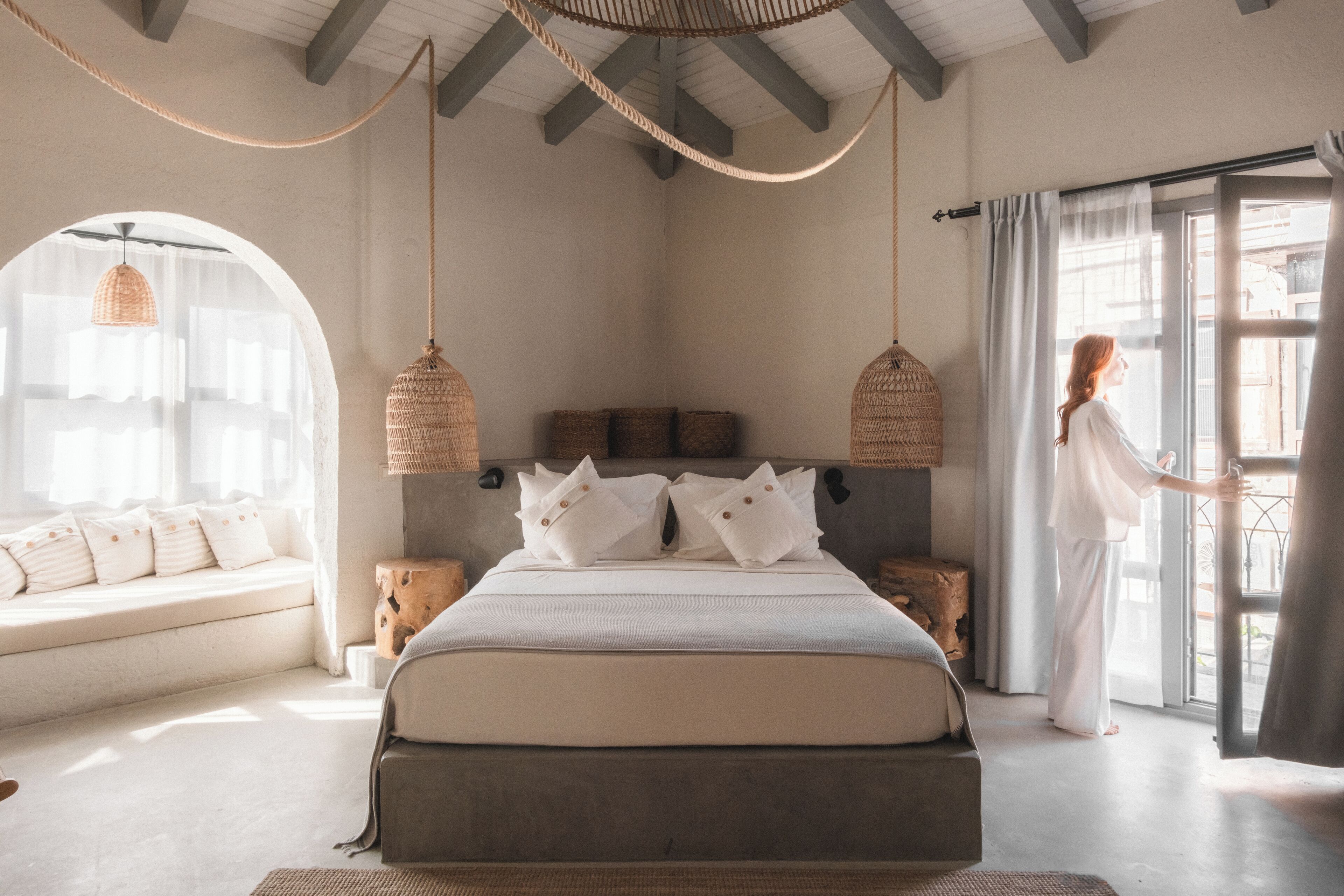 Un dormitorio con una cama grande, dos lámparas de mimbre colgantes, una ventana con cortinas y vistas al exterior.