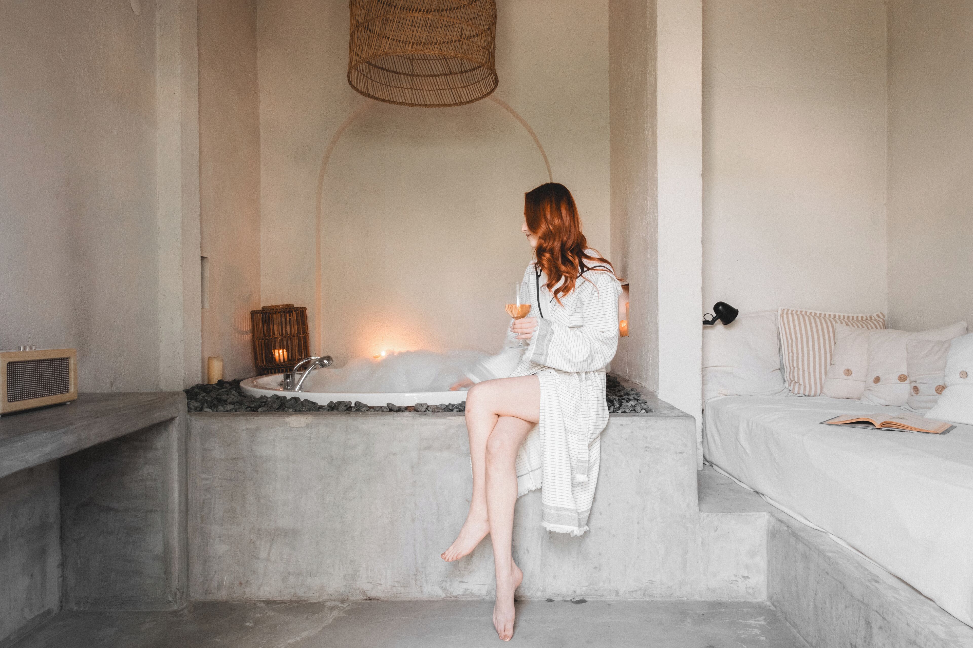 Una mujer sentada junto a una bañera en un ambiente de spa, con una cama y un libro encima.