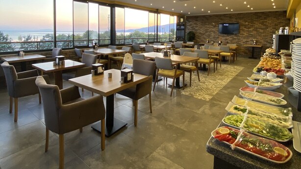 Un amplio comedor interior con techos altos, grandes ventanales que ofrecen vistas de la ciudad y una barra de buffet con diversas opciones de comida.