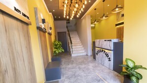 Zona de recepción de un hotel con piso de mármol, mostrador de recepción, una escalera y señalización de recepción.